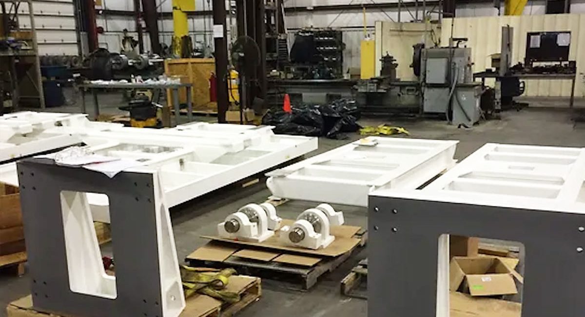 Built-to-Print-Defense Custom-built industrial components and machinery parts organized in a manufacturing facility with heavy-duty equipment in the background